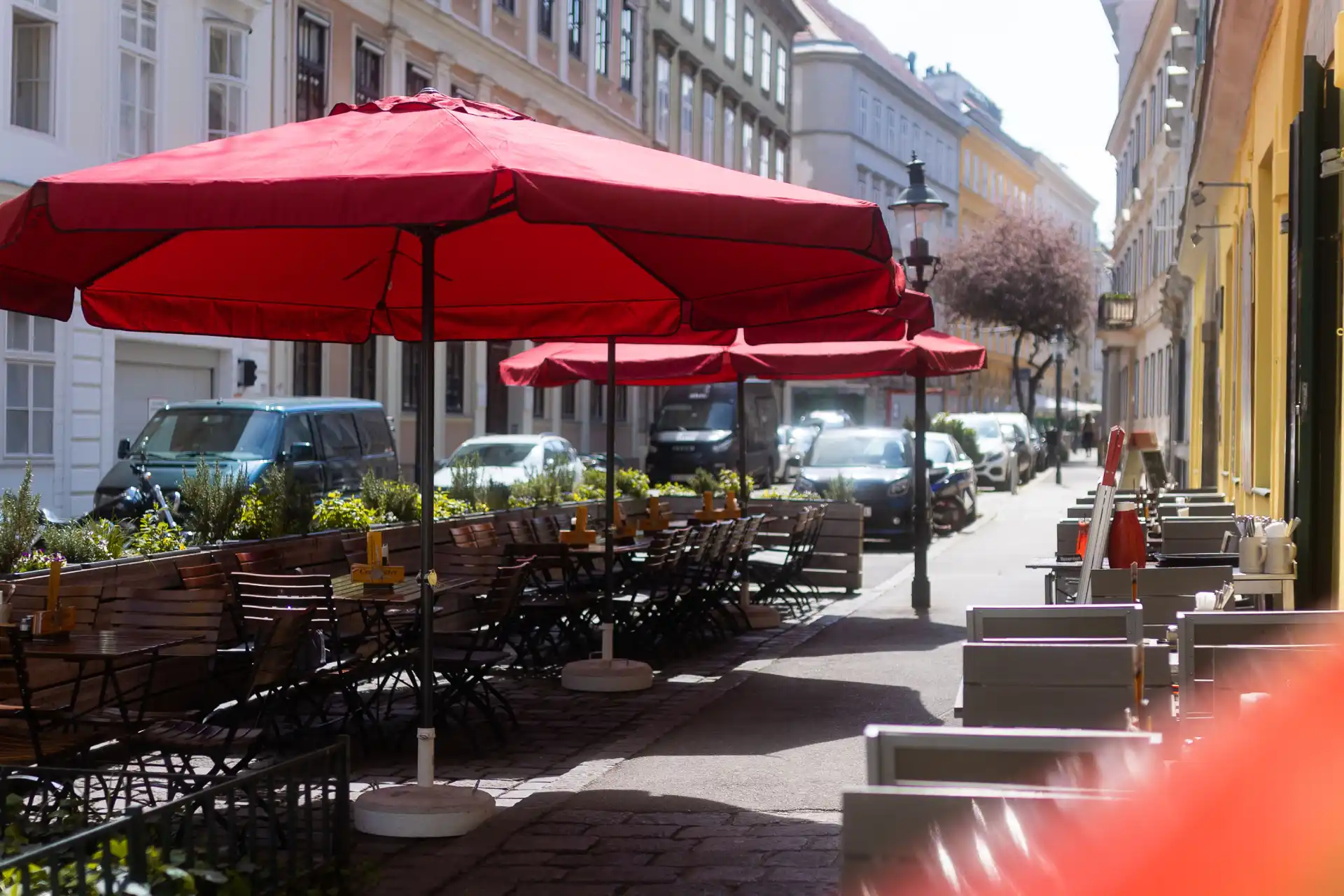Außenansicht eines Restaurants Namens Centimeter mit roten Sonnenschirmen und Sitzplätzen im Freien im Gastgarten Wien, gemütlicher Gastgarten vor einem Lokal in einer Wiener Altbaustraße.